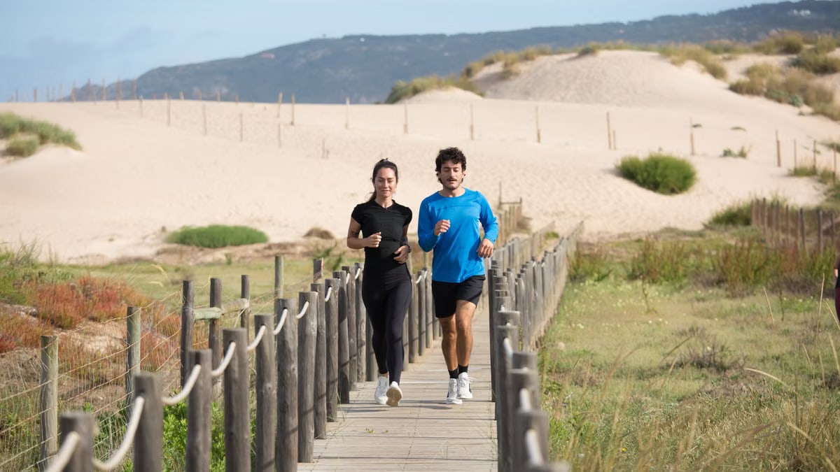 A couple enjoying jogging on a scenic boardwalk by sand dunes in Portugal.